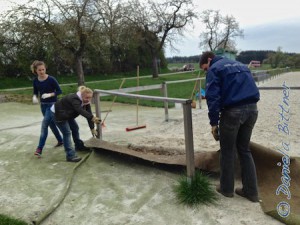 Durch den regen Reitbetrieb hat der Teppich um den Reitplatz Falten geschlagen. Mit vereinten Kräften wird der Teppich wieder gerade gezogen...