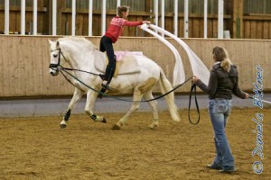 Charlotte führt auf ihrem Schimmel Jacko eine Voltikür im Galopp vor als Mond und schwenkt dabei auch Bänder!